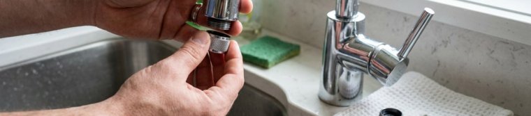 Hands unscrewing the aerator from a kitchen faucet