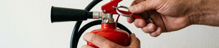 Hands pulling the safety pin from a red fire extinguisher
